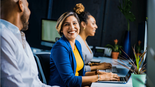 A healthcare professional smiling while working on a laptop in a modern office