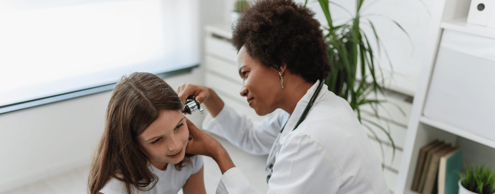 A licensed vocational nurse in a white coat examining a young patient's ear during a clinical visit